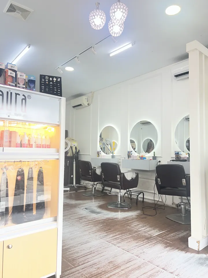 Sudut interior salon dengan cermin bulat, kursi hitam, dan lantai bernuansa kayu