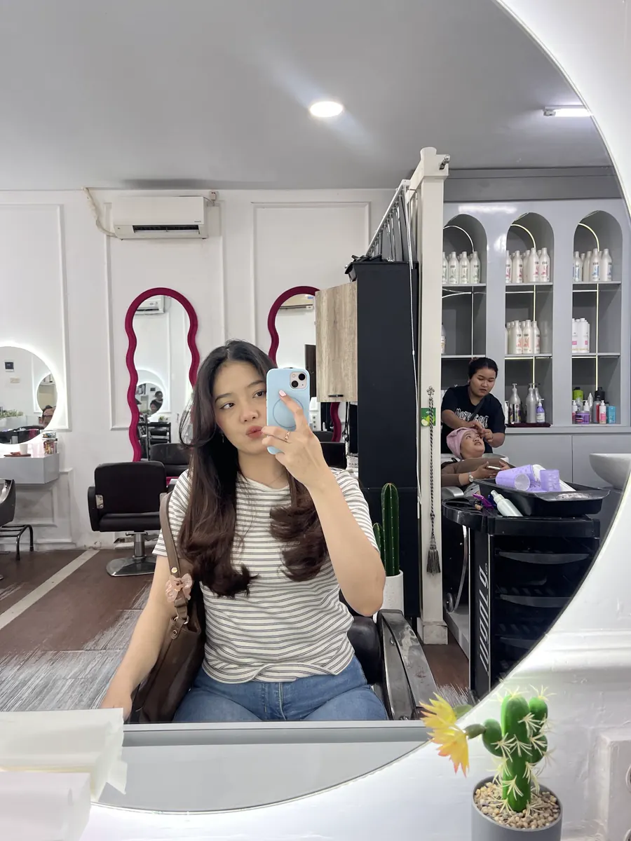 Pelanggan berambut panjang di depan cermin salon, dengan bingkai cermin merah anggur di belakangnya